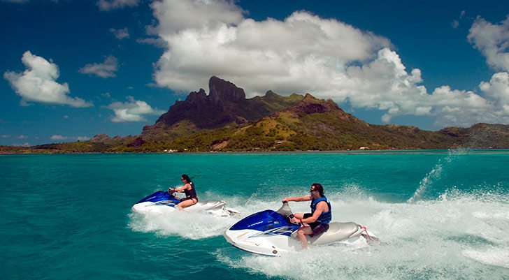 Two jet ski riders in front of a tropical rocky island