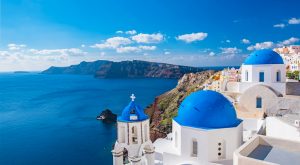 Iconic Greek blue-domed, white buildings overlook the water in The Cyclades, an island group in the Aegean Sea, southeast of mainland Greece