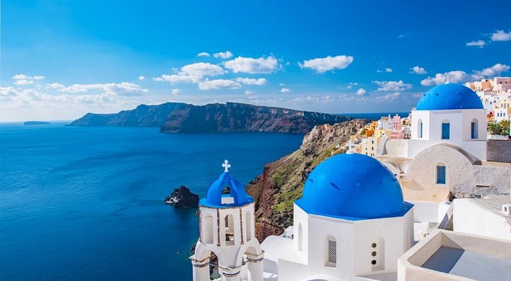Iconic Greek blue-domed, white buildings overlook the water in The Cyclades, an island group in the Aegean Sea, southeast of mainland Greece