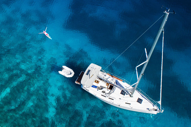 Aerial view of sailing yacht and swimming woman in clear Caribbean water.