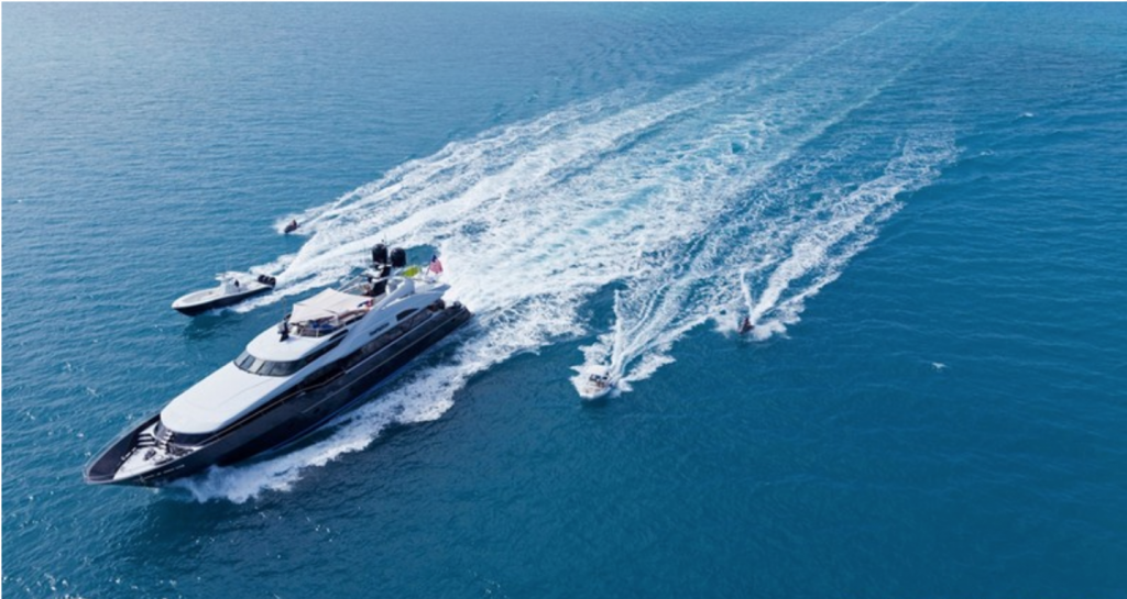 123ft motor yacht TEMPTATION traveling fast on the water, flanked by toys and tenders