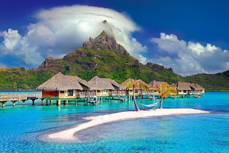 Hammock between two palm trees near cottages on stilts in Bora Bora, French Polynesia blue water mountain peak with clouds