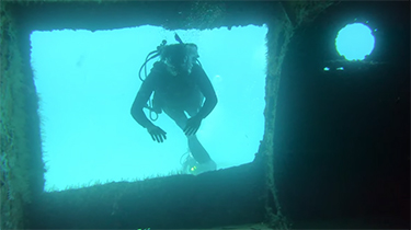 SCUBA diver swimming through hole in underwater shipwreck off sail catamaran LOLALITA in the British Virgin Islands