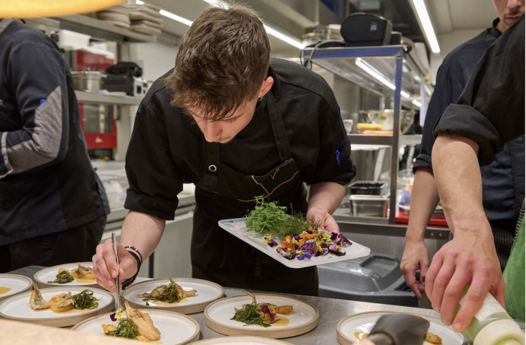 Chef adding greens and flowers to dish at MEDYS Chefs Competition 2023 in Nafplion, Greece