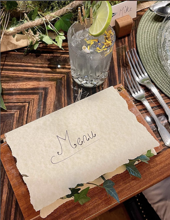 Placesetting with menu on parchment filled with ivy and a cocktail w lime slice and a paper straw photo©oatsakellari